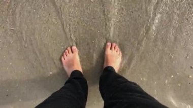 Mens ayakları sahildeki deniz dalgalarını yıkıyor.