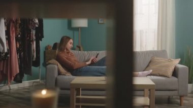 Genç kız kanepede uzanıyor ve video bağlantısıyla telefonla konuşuyor.