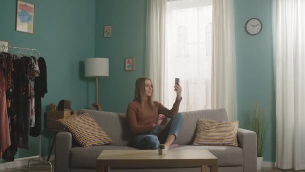 Young girl is sitting on a sofa and talking on the phone via video link — Stock Video