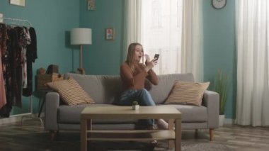 Genç bayan telefonda bir şeye bakıyor ve neşeli duygular ifade ediyor.