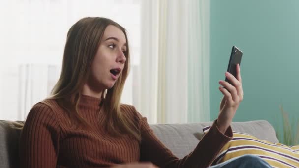 Ung flicka sitter på en soffa och pratar på ett videosamtal — Stockvideo