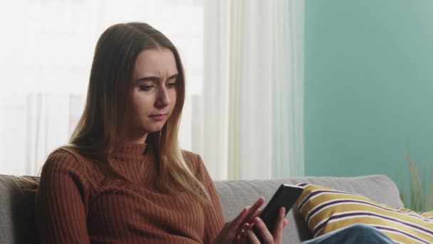 Jeune fille assise sur le canapé avec un téléphone dans ses mains — Video