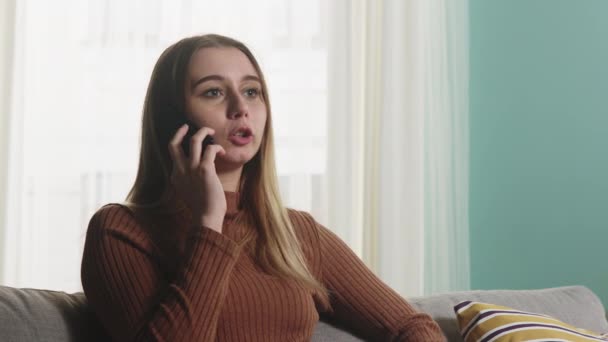 Flickan sitter på en soffa och pratar i telefon. Närbild — Stockvideo
