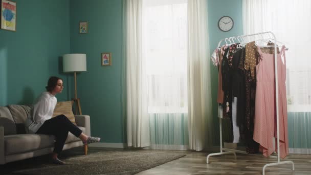 Ung kvinna stiger upp från soffan och väljer en klänning — Stockvideo
