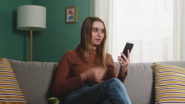 Jovem está sentada em um sofá e falando em uma chamada de vídeo — Vídeo de Stock