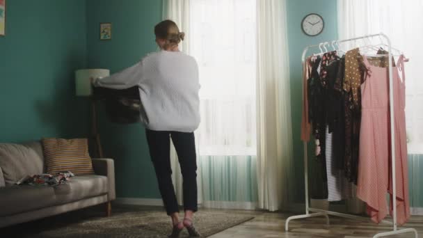 Jong meisje in een witte trui strooit kleding rond de kamer — Stockvideo