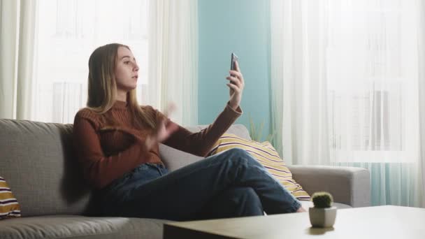 Mädchen sitzt auf einem Sofa und spricht per Videoanruf — Stockvideo