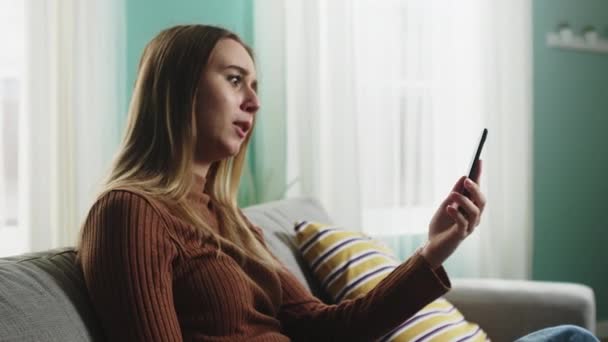 Mladá dívka sedí na pohovce a mluví na videohovoru — Stock video