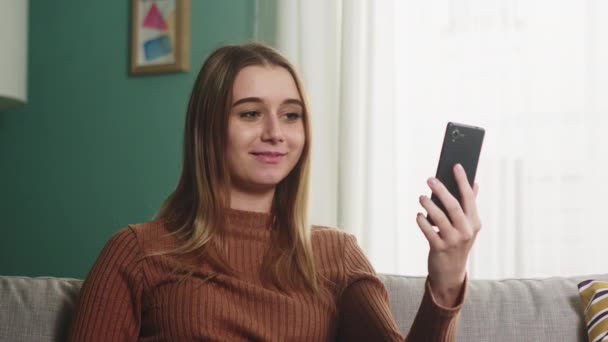 Flickan sitter på en soffa och pratar på ett videosamtal — Stockvideo