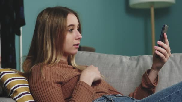 Молода дівчина лежить на дивані і розмовляє на відеодзвінок — стокове відео