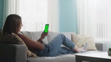 Genç bayan bej bir kanepede uzanıyor ve video görüşmesinde konuşuyor. Kromakey