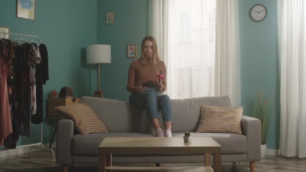 Ung kvinna sitter på baksidan av soffan och tar en selfie — Stockvideo