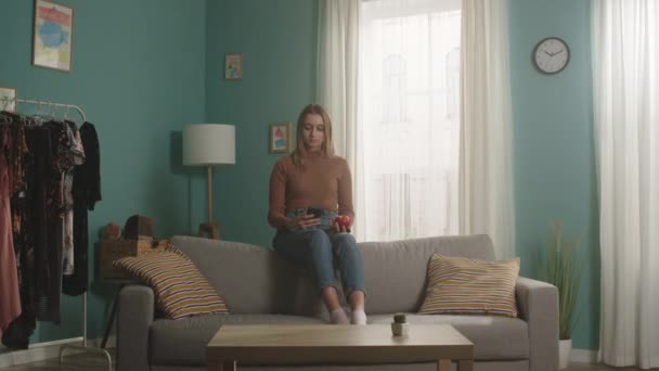 Девушка садится на спинку дивана и делает селфи — стоковое видео