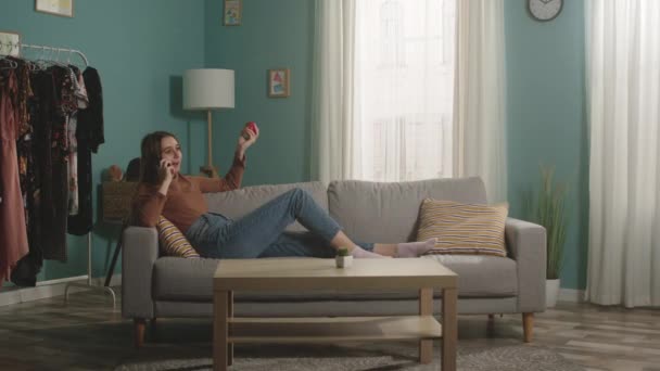 Женщина с красным яблоком лежит на диване и разговаривает по телефону — стоковое видео