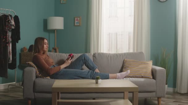 Девушка с красным яблоком лежит на диване и делает селфи — стоковое видео