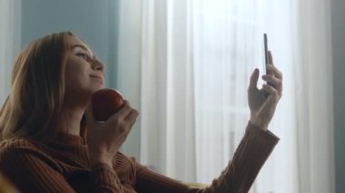 Kırmızı elmalı güzel bir kadın cep telefonuyla selfie çekiyor.