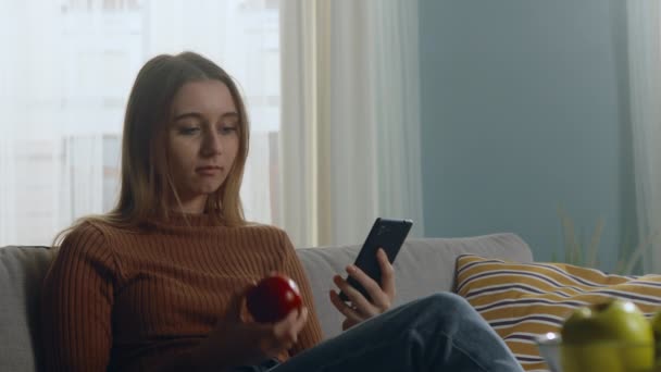 Mooi meisje bijt rode appel en kijken naar iets op telefoon — Stockvideo