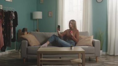 Kırmızı elmalı genç bayan kanepede oturur ve cep telefonuyla selfie çeker.