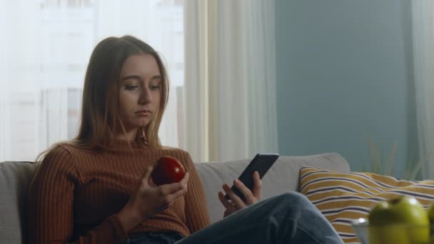 Vacker dam biter rött äpple och tittar på något på telefonen — Stockvideo