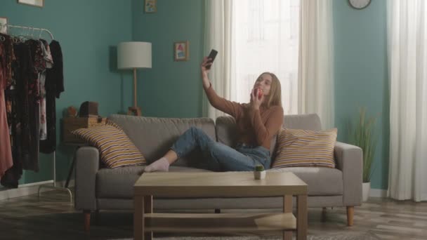 Νεαρή κοπέλα με κόκκινο μήλο κάθεται στον καναπέ και βγάζει selfie στο κινητό — Αρχείο Βίντεο