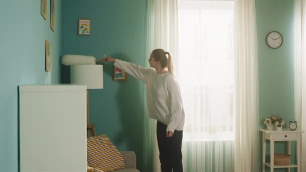 Jonge vrouw in witte trui veegt stof van meubels. — Stockvideo