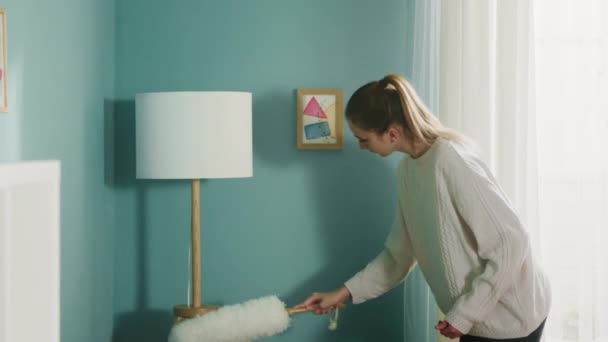 Jeune femme en pull blanc essuie la poussière des meubles. — Video