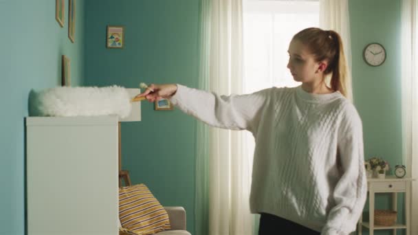 Egy fiatal hölgy fehér pulóverben letörli a port a bútorokról.. — Stock videók