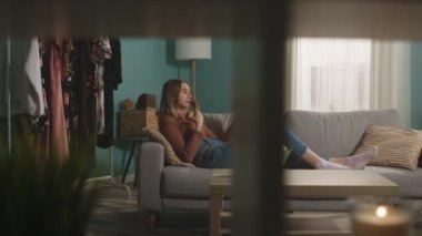 Genç bir kadın kanepede uzanmış kırmızı bir elma yiyor ve video bağlantısıyla konuşuyor.