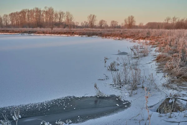 Breath of winter, first ice on the lake, dawn on a frosty morning with frost on the grass, close-up of frost, patterns on the first ice. Winter