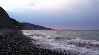 Sakin denizin üzerinde gün doğumu, bulutların arasından bulutların içine, sakin deniz manzarasına doğru süzülen turuncu ışık huzmeleri saçar..