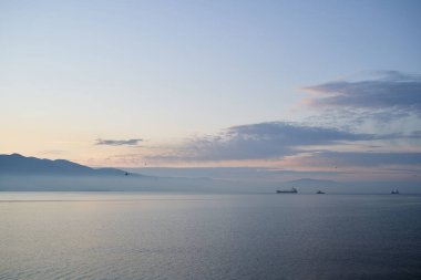 Sakin denizin üzerinde gün doğumu, bulutların arasından bulutların içine doğru süzülen, sakin deniz manzarasına doğru turuncu ışık huzmeleri saçar.,