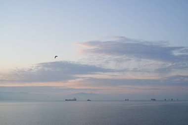 Sakin denizin üzerinde gün doğumu, bulutların arasından bulutların içine doğru süzülen, sakin deniz manzarasına doğru turuncu ışık huzmeleri saçar.,
