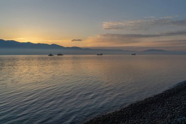 Sakin denizin üzerinde gün doğumu, bulutların arasından bulutların içine doğru süzülen, sakin deniz manzarasına doğru turuncu ışık huzmeleri saçar.,