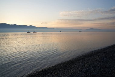 Sakin denizin üzerinde gün doğumu, bulutların arasından bulutların içine doğru süzülen, sakin deniz manzarasına doğru turuncu ışık huzmeleri saçar.,