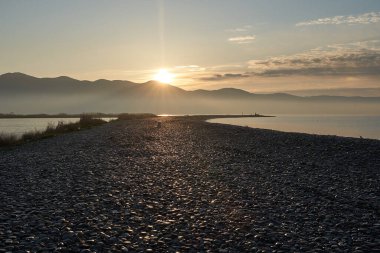 Sakin denizin üzerinde gün doğumu, bulutların arasından bulutların içine, sakin deniz manzarasına, denize doğru, turuncu ışık huzmeleri saçar..