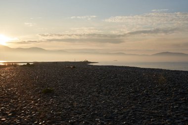 Sakin denizin üzerinde gün doğumu, bulutların arasından bulutların içine, sakin deniz manzarasına, denize doğru, turuncu ışık huzmeleri saçar..