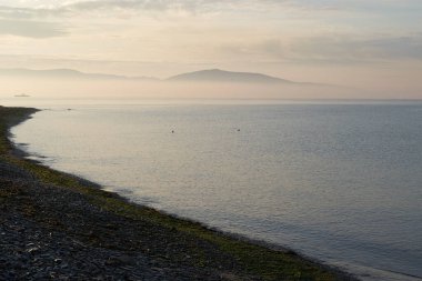 Sakin denizin üzerinde gün doğumu, bulutların arasından bulutların içine, sakin deniz manzarasına, denize doğru, turuncu ışık huzmeleri saçar..