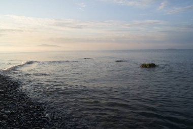 Sakin denizin üzerinde gün doğumu, bulutların arasından bulutların içine, sakin deniz manzarasına, denize doğru, turuncu ışık huzmeleri saçar..