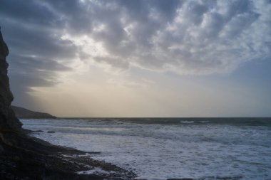 Sakin denizin üzerinde gün doğumu, bulutların arasından bulutların içine, sakin deniz manzarasına, denize doğru, turuncu ışık huzmeleri saçar..