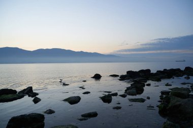 Sakin denizin üzerinde gün doğumu, bulutların arasından bulutların içine, sakin deniz manzarasına, denize doğru, turuncu ışık huzmeleri saçar..