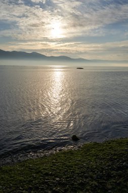 Sakin denizin üzerinde gün doğumu, bulutların arasından bulutların içine, sakin deniz manzarasına, denize doğru, turuncu ışık huzmeleri saçar..