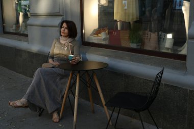 Woman sits in a sidewalk cafe chair with a cup of morning coffee