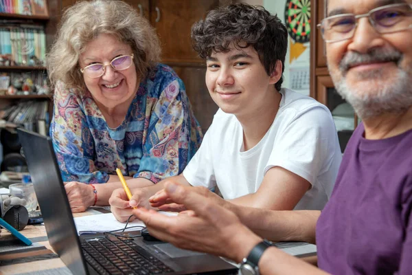 Avós e adolescente em casa reunidos em torno do laptop sorrindo — Fotografia de Stock
