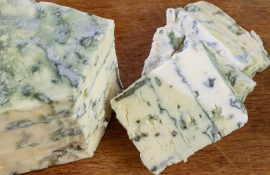 Tahta kesme tahtasının üzerinde mavi peynir dilimleri ve çubuklar.