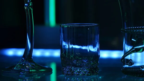 Glasses and shots highlighted by green light on a black background. Low key. — Stock Photo, Image