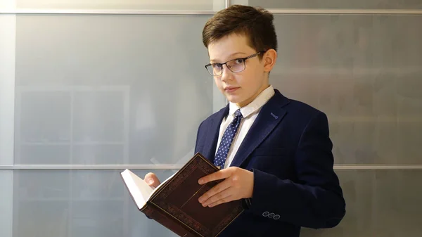 Gözlüklü okul çocuğu elinde bir kitap tutuyor..