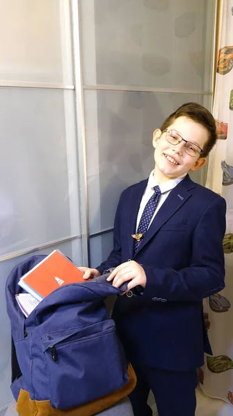 Okul üniformalı ve gözlüklü çocuk okul için bir çanta topluyor.