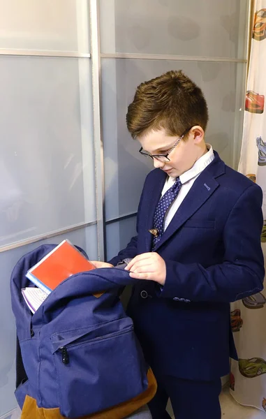 Okul üniformalı ve gözlüklü çocuk okul için bir çanta topluyor.