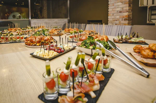 Lezzetli yemek ve atıştırmalıklarla dolu bir restoran masası. Burgerler, salatalar, aperatifler, peynirler, salamlar, meyveler. Masa yemek için hazır.
