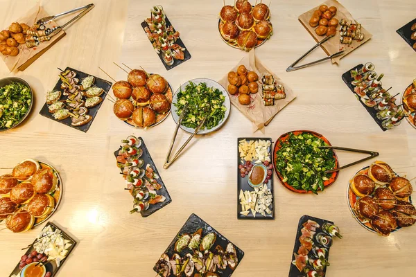 Lokantadaki modern lezzetli yiyeceklerle dolu bir masa. Hamburgerler, atıştırmalıklar, mezeler, salatalar ve peynirler.